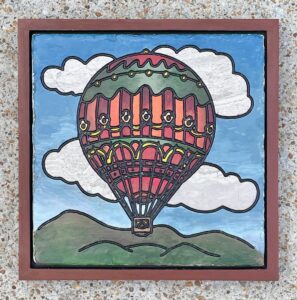 Marble tile with a hot air balloon floating over a landscape engraved and painted on it