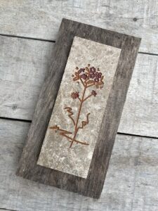 Marble tile mounted on wood with a stylized flower engraved and painted on it.
