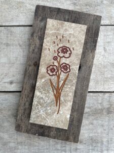 Marble tile mounted on wood with a stylized flower engraved and painted on it.