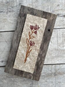 Marble tile mounted on wood with a stylized flower engraved and painted on it.