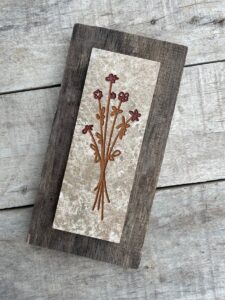 Marble tile mounted on wood with a stylized flower engraved and painted on it.