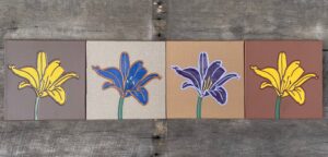 Four quarry tiles with an identical lily image engraved on each and painted differently.