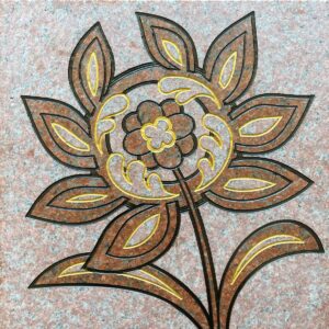 Red granite tile with a stylized flower engraved and painted on it.