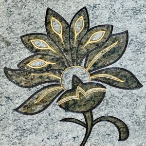 Green granite tile with a stylized flower engraved and painted on it.