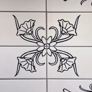 Backsplash detail - Floral design engraved on white subway tile, colored with black lacquer Four white subway tiles engraved with a partial floral design, placed together to make a complete image, painted black.