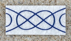 4in. x 8in. engraved white marble tiles aligned in a pattern White marble tile with a design engraved and painted in blue on it.